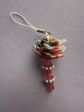 A decorative rose-shaped charm with a white cord loop, featuring layered pink and white petals with metallic gold glitter accents and a pink stem decorated with small white beads, shown on a textured gray background.