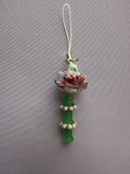 A decorative charm featuring a green bamboo stem with white pearl-like beads, a pink and white flower, a small white bird, and a white loop at the top, shown against a textured gray background.