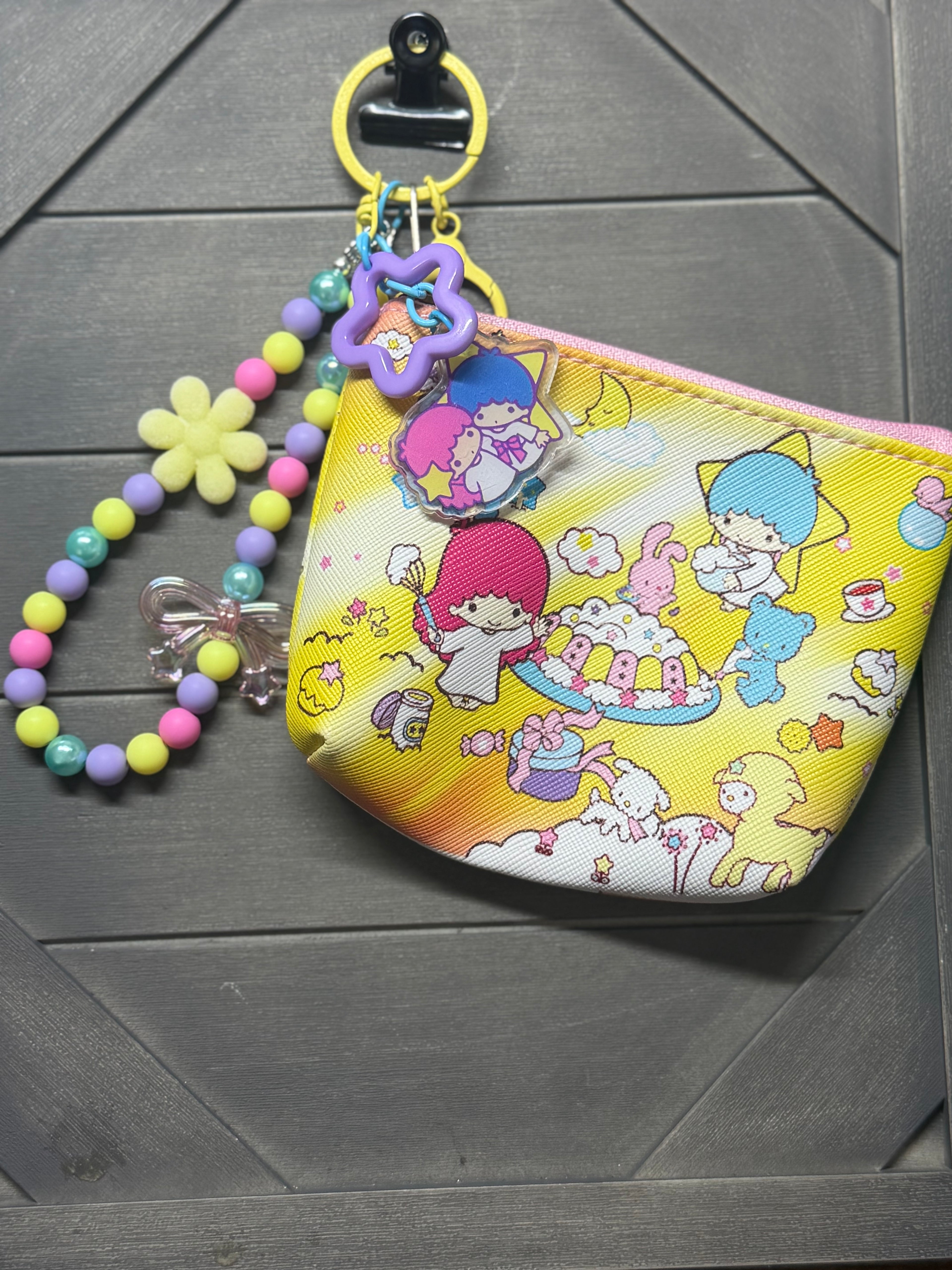 A yellow Star Party coin purse with a colorful beaded strap and character charms, displayed on a dark gray wood background.