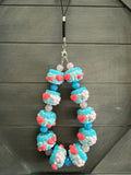 A beaded necklace or phone strap charm featuring light blue and pink 3D cupcake beads with red hearts, suspended from a black cord with silver hardware, set against a dark gray wood background.