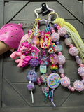 A pastel pink and purple My Little Pony themed beaded keychain set with a pink pony charm, a ice cream-shaped accessory, and a yellow tassel, displayed on a dark wood background.
