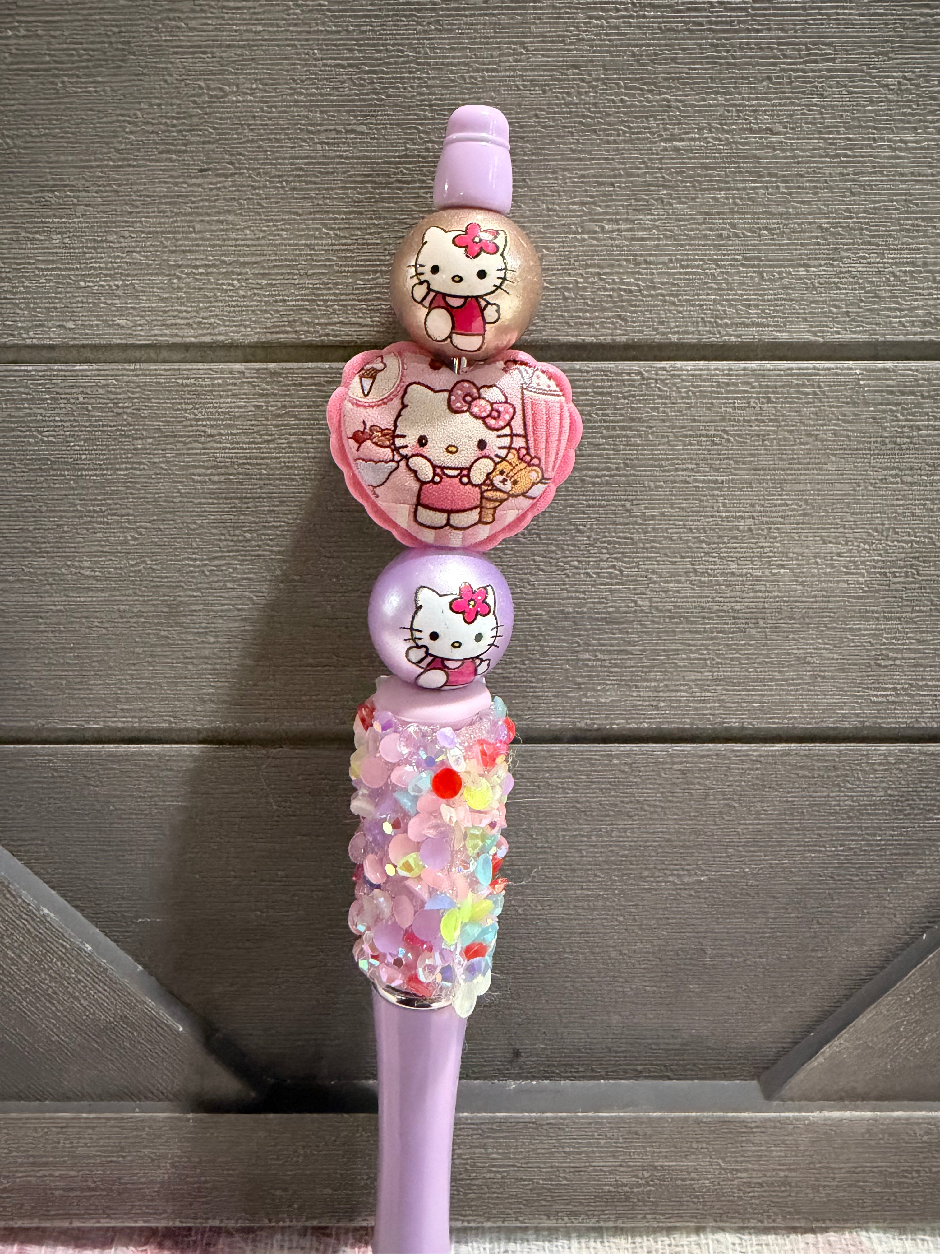A pink Hello Kitty toothbrush with decorative beads, a heart-shaped charm, and a glittery handle, shown against a gray wooden background.