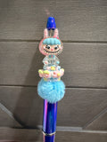 A decorative blue pen with a cartoon bunny character on top, surrounded by pastel flowers and a fluffy light blue pom-pom, set against a dark gray paneled background.